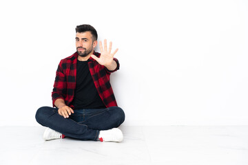 Young handsome man sitting on the floor counting five with fingers