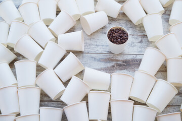 White paper cups scattered on the table and one with coffee beans among them