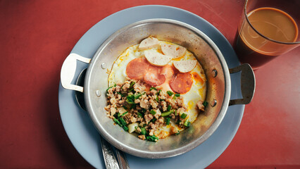 Food set of breakfast pan-fried egg with toppings sausage and vegetables on small pan at local restaurant cafe shop in Thailand