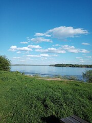 river blue sky clouds green grass embankment