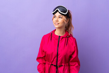 Skier teenager girl with snowboarding glasses over isolated purple background thinking an idea while looking up