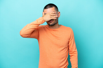 Young caucasian man isolated on blue background covering eyes by hands. Do not want to see something