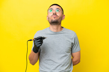 Tattoo artist caucasian man isolated on yellow background and looking up