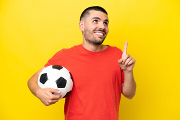 Young caucasian man playing soccer isolated on yellow background pointing up a great idea