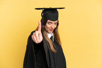 Young university graduate isolated on yellow background showing and lifting a finger