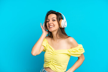Fototapeta premium Young caucasian woman isolated on blue background listening music