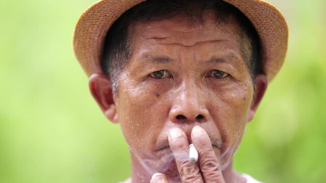 candid portrait of asian male with serious look smoking tobacco looking at camera