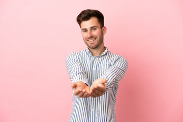 Young caucasian handsome man isolated on pink background holding copyspace imaginary on the palm to...