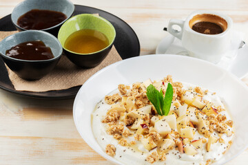 Yogurt with flakes, fruits and cup of coffee on white wooden background. Βreakfast concept.
