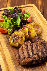 Grilled Rib Eye Black Angus served with fries, green salad and sauce on wooden background.