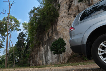 Beside of grey car can see with glass and wheels. Parking in the park. Background of dirt roads and high mountains and forests.
