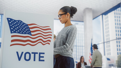 Young Stylish African American Female Casting Her Vote at a Polling Station and Putting Her Ballot...