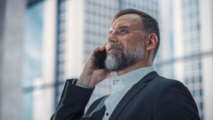 Confident Middle Aged Businessman in a Suit Standing in Modern Office, Answering a Phone Call,...