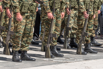 Soldiers stand in row with a guns in hand in camouflage uniforms.