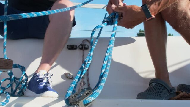 Men diligently untangle ropes on sitting deck of ship. Sport enthusiasts prefer water activities while on summer vacation