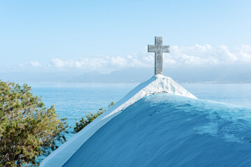 Stone cross over the white Greek church in blue sky.
