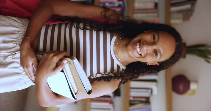 Vertical view of happy African gen Z girl holding workbooks, textbook visiting public library for exams preparations, posing, smiling, looking at camera. Higher education, excellent student portrait