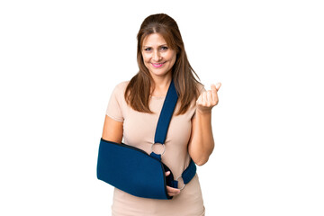 Middle age with broken arm and wearing a sling over isolated background making money gesture