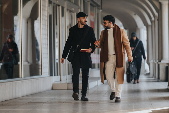 An image depicting two stylish businessmen engaged in a discussion while walking through an urban corridor. They exude confidence and professionalism.