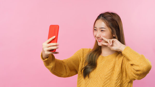 Young women smile to selfie with v sign on smartphone with empty space on isolated pink background
