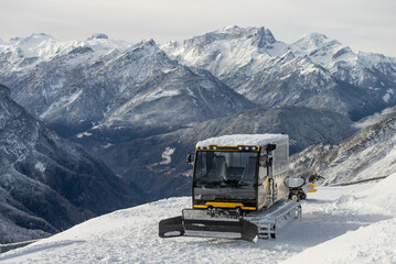 Piste groomer in front of the Mountains Dolomites alps  Italy. Snow groomer in dolomites alps in Italy. snow groomer in winter mountains. - obrazy, fototapety, plakaty