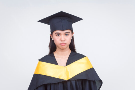 Stoic female filipino graduate wearing a black cap and gown with a yellow stole, ready for the ceremony.