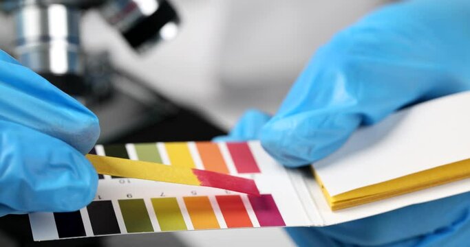 Scientist chemist holding ph test in hands and comparing result closeup. Acid-base balance test strip and test solution