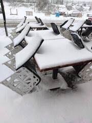 Snow covered chairs and table at closed cafe, coffee shop.