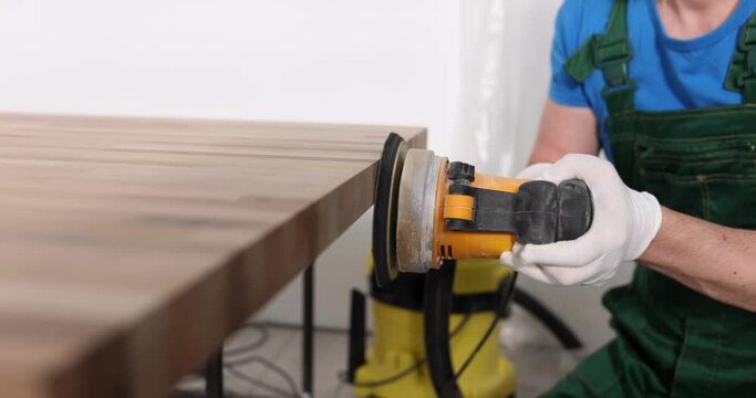 Carpenter uses an orbital sander to polish wood in workshop. DIY manufacturer and woodworking concept