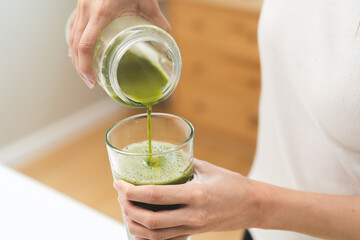 Detox juice concept, Hand of woman, girl holding bottle making green vegetable smoothie pouring in...