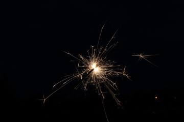 A sparkler illuminates dark evening - bright, golden sparks fly - celebration holiday - new years...