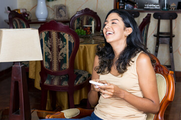 happy black haired latin woman chatting with her smartphone from her living room