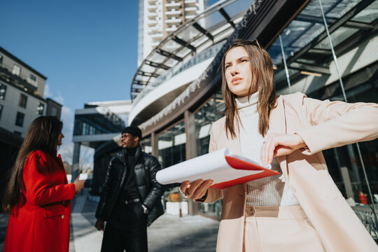Stunning businesswoman in a smart casual outfit outside, reviewing documents in a red folder, with a focused expression.