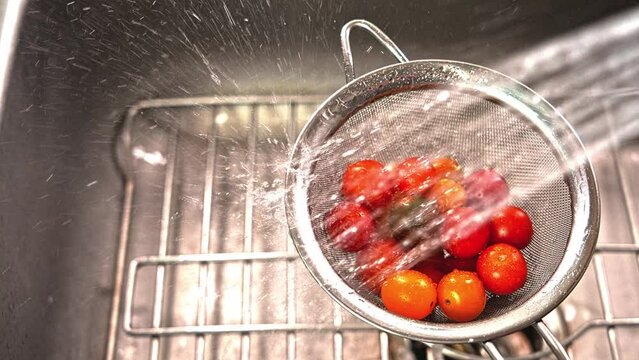 Washing little tomatoes inside strainer with riser hose in sink in sink slow motion video