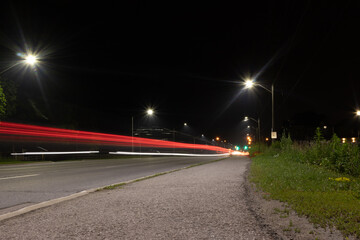 Nighttime cityscape - bright streetlights - red and white light trails streak across the road - passing vehicles long exposure. Taken in Toronto, Canada.