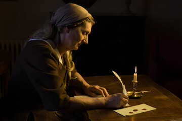 Lady in medieval costume writing a letter with a feather quill - 727214678