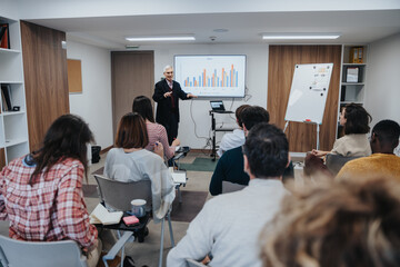 Engaged audience listening intently to a senior businessman offering insights during a corporate training session, in a well-lit modern office environment.