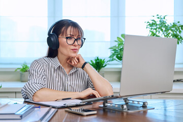 Middle-aged woman in headphones working at computer in home office