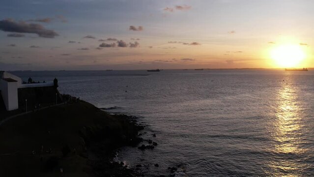 Ships passing in the background of the Barra Lighthouse / Stronghold during sunset while a large group watches