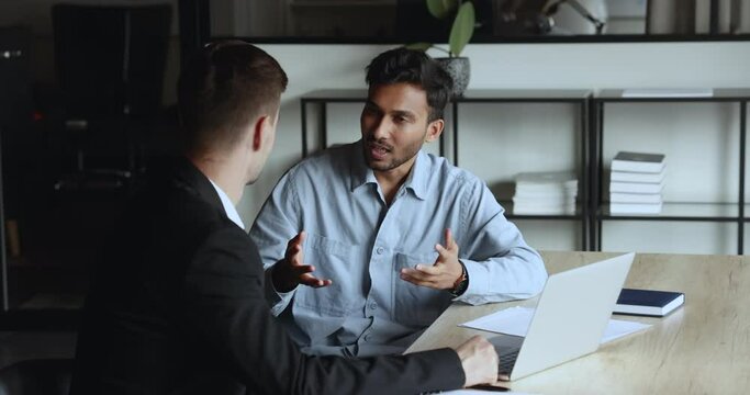 Two happy diverse business partners men shaking hands, smiling, discussing teamwork, partnership, getting successful job result, agreement. Indian project manager talking to investor at table