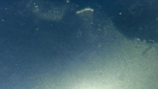 Underwater view of spring ice drift, thin crystalline ice with air bubbles frozen into it quickly moves downstream in rays of morning light, Slow motion. Thin spring ice floating on blue sky backgroud
