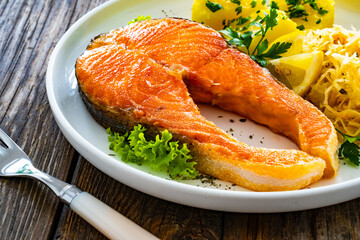 Fried salmon steak with boiled potatoes and sauerkraut on wooden table
