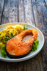 Fried salmon steak with boiled potatoes and sauerkraut on wooden table
