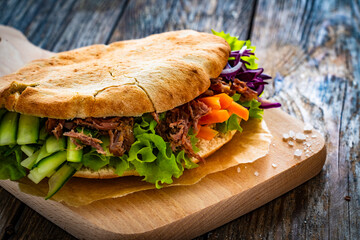 Pita - big sandwich with pulled beef and fresh vegetables on wooden table
