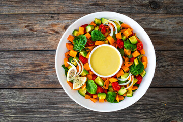 Tasty salad - baked sweet potatoes, avocado, spinach and tomatoes with tahini sauce on wooden table
