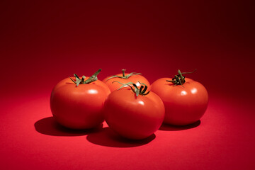 Four red tomato with a green stalk, on a red background.