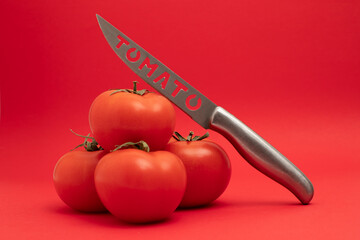 Knife with the inscription Tomato  lies on the tomato vegetable isolated over red background.