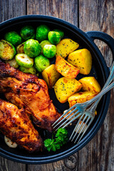 Cooked rabbit thighs with potatoes and brussels sprout in frying pan
