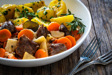 Roast pork cheeks with carrots and celeriac in sauce with boiled potatoes on wooden table 