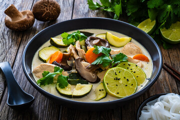 Tom Kha Gai soup - Thai soup with chicken breast nuggets and noodles on wooden table